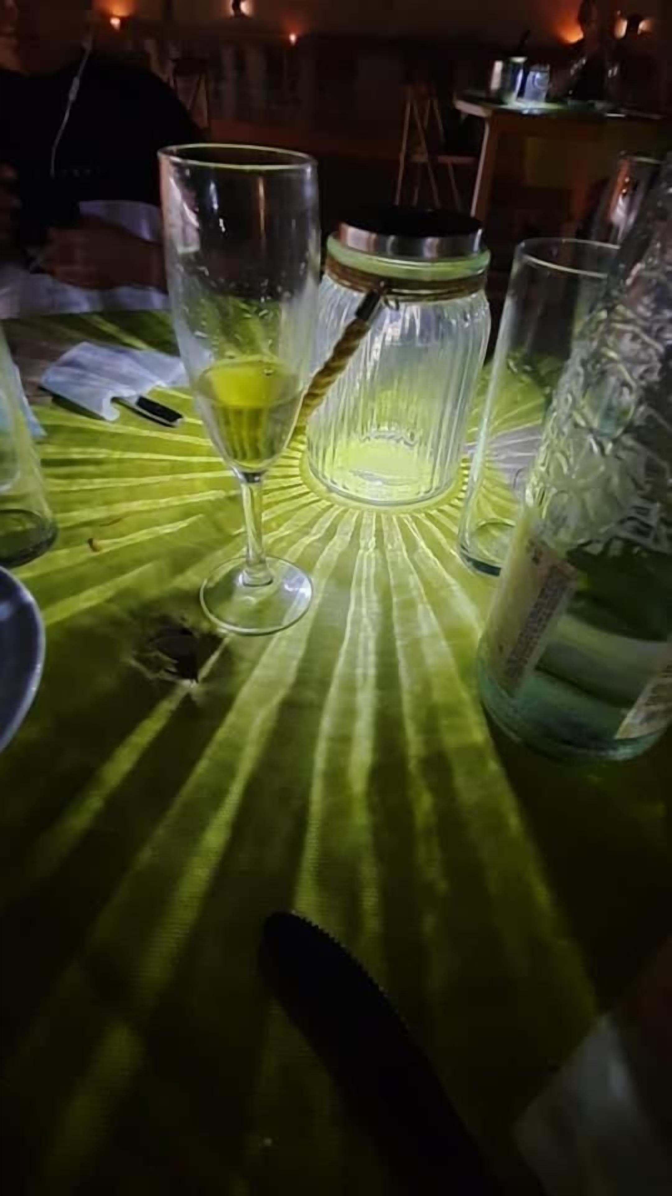 Una mesa con mantel verde, un vaso con líquido amarillo y una botella.