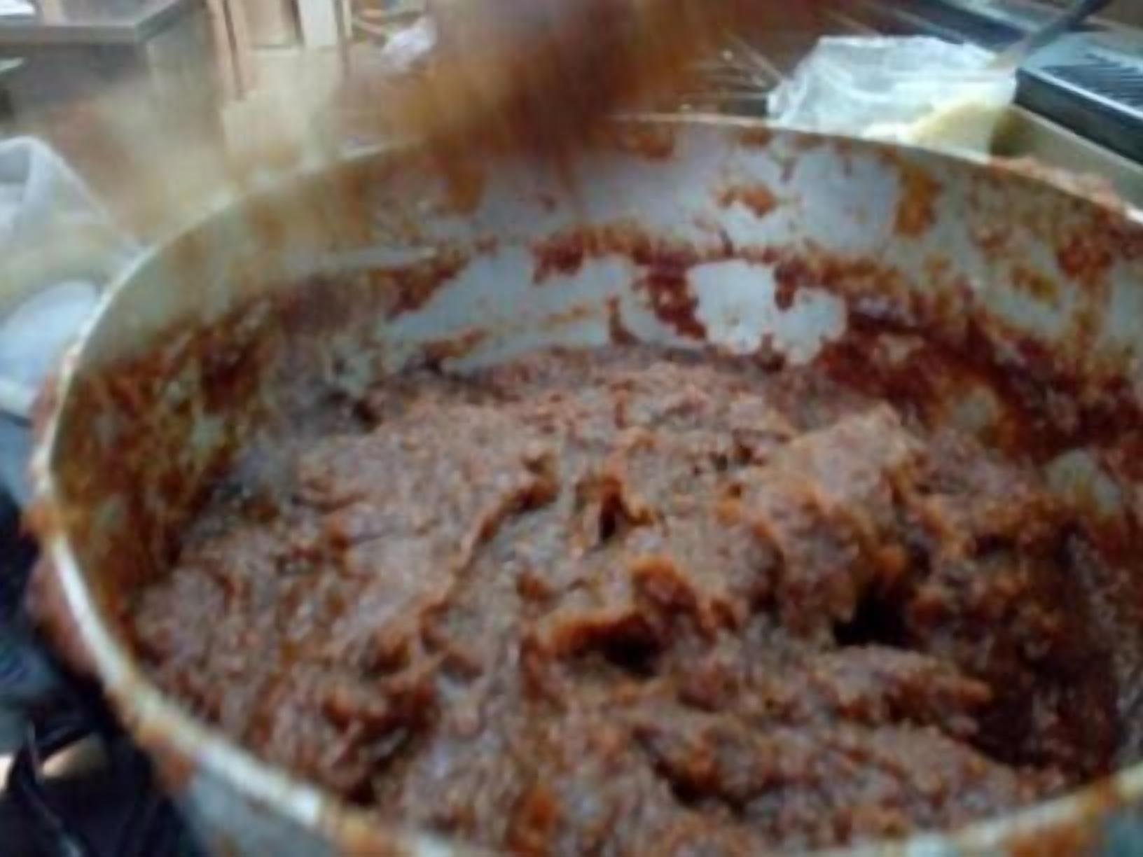 A pot of stew or sauce with a thick, brown consistency, possibly simmering on a stove.