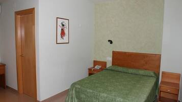 Une chambre à coucher avec un lit, une porte en bois, une table de chevet avec un téléphone et un tableau encadré au mur.