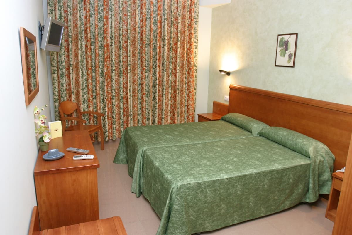 A hotel room with a wooden bed, a desk with a chair, a small table, a TV, and a curtain with a floral pattern.