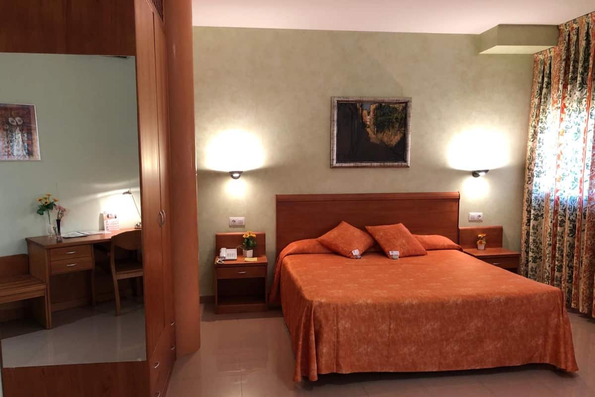 A hotel room with a bed, a desk, and a chair. There are two bedside tables with lamps.