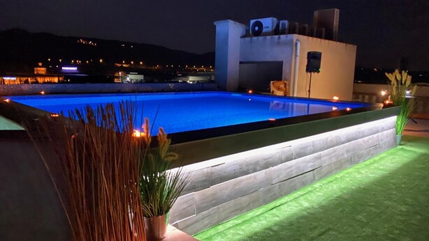 Une piscine au design moderne, entourée d’une terrasse bien aménagée et agrémentée de plantes et de bougies.