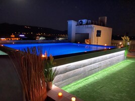 Una piscina de diseño moderno, rodeada por una terraza bien iluminada con plantas y velas.