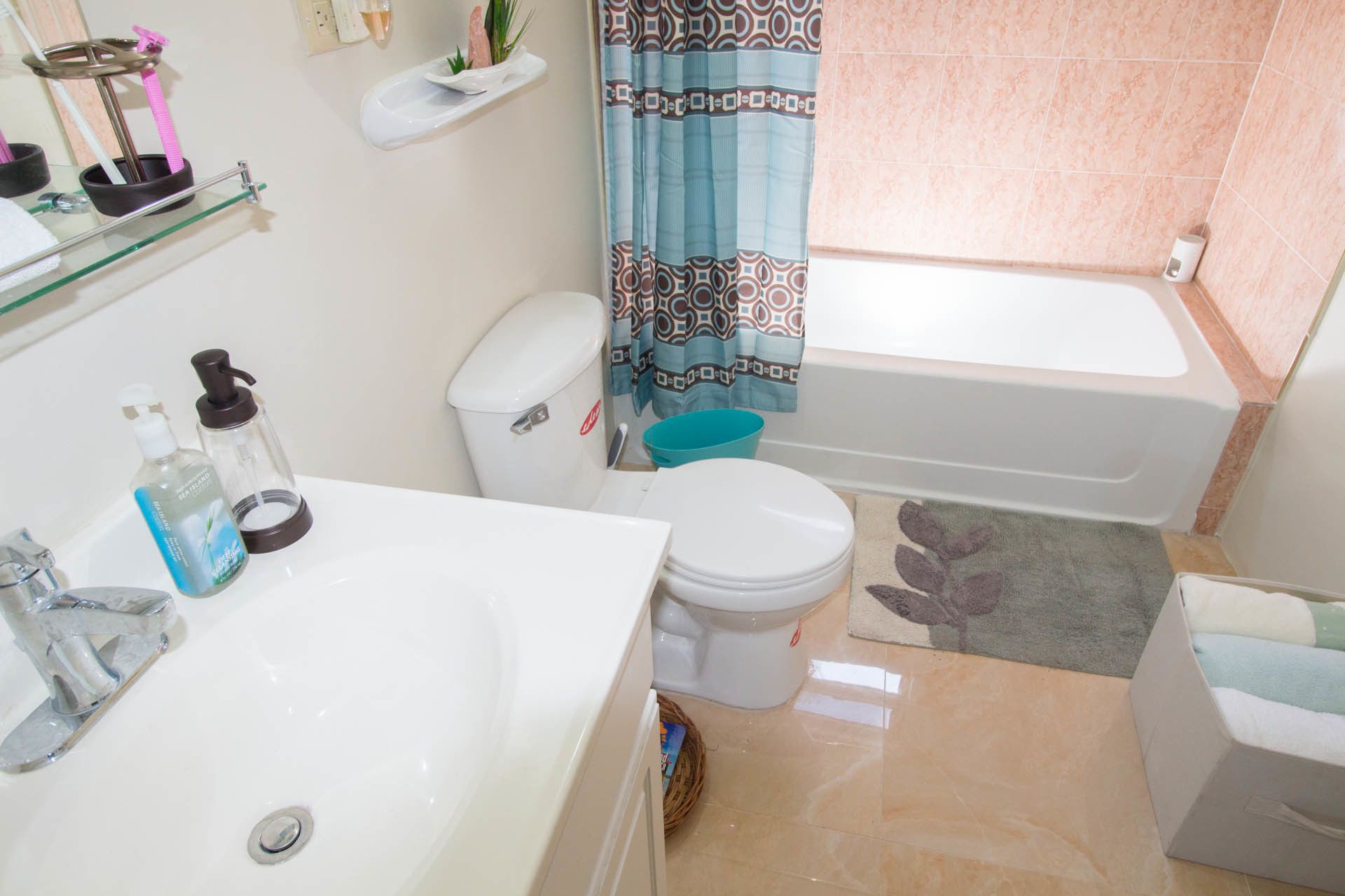 A bathroom with a white sink, toilet, and bathtub. There are shelves with toiletries and a blue shower curtain.