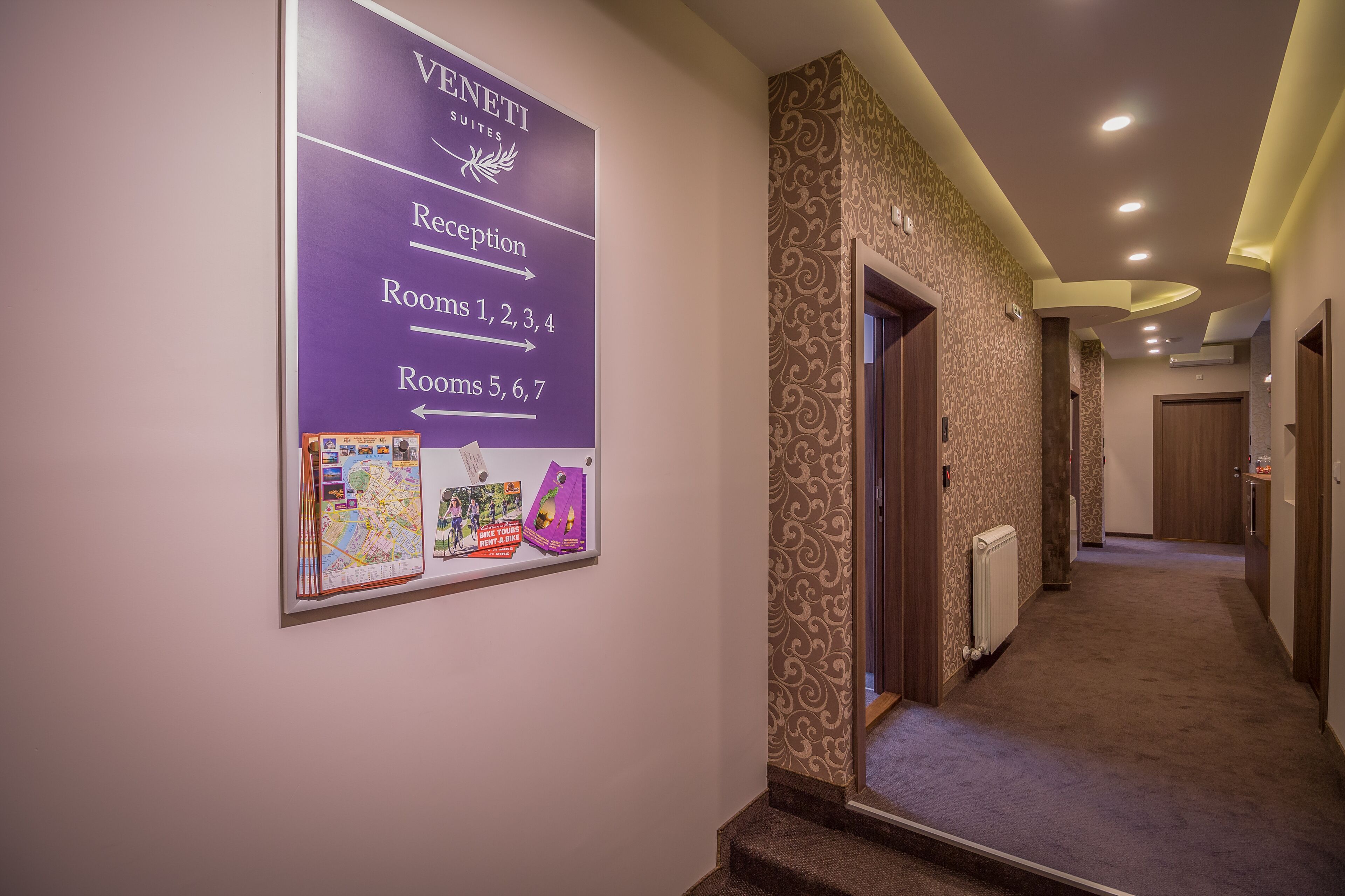 A hotel hallway with a reception sign, directional arrows to rooms, and a carpeted floor.