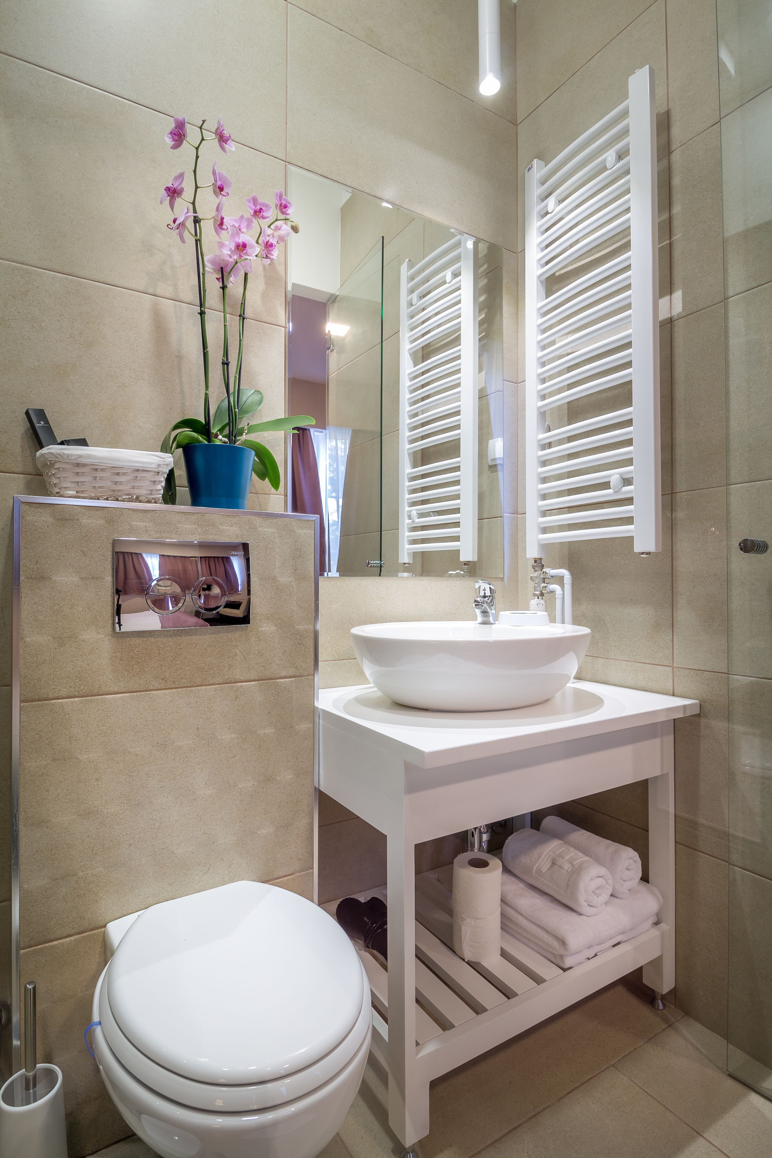 Une salle de bain moderne avec un lavabo blanc, des toilettes, un miroir et une plante en pot.