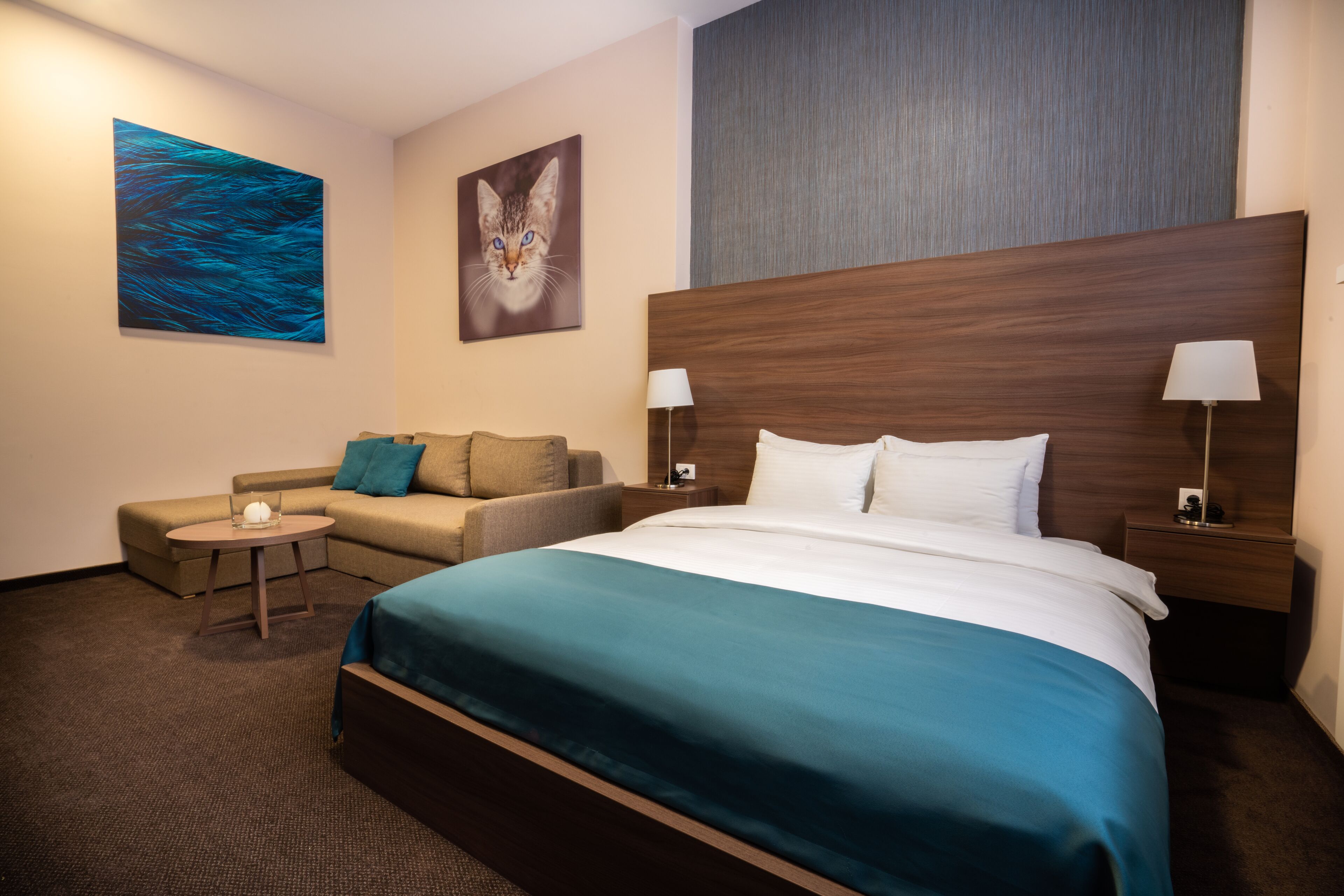 Habitación de hotel con una cama grande, un sofá, una mesita pequeña y dos mesitas de noche con lámparas.