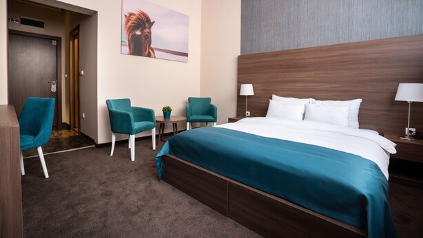 A hotel room with a large bed, two chairs, a small table, and a painting on the wall. - Veneti Suites (Belgrade)