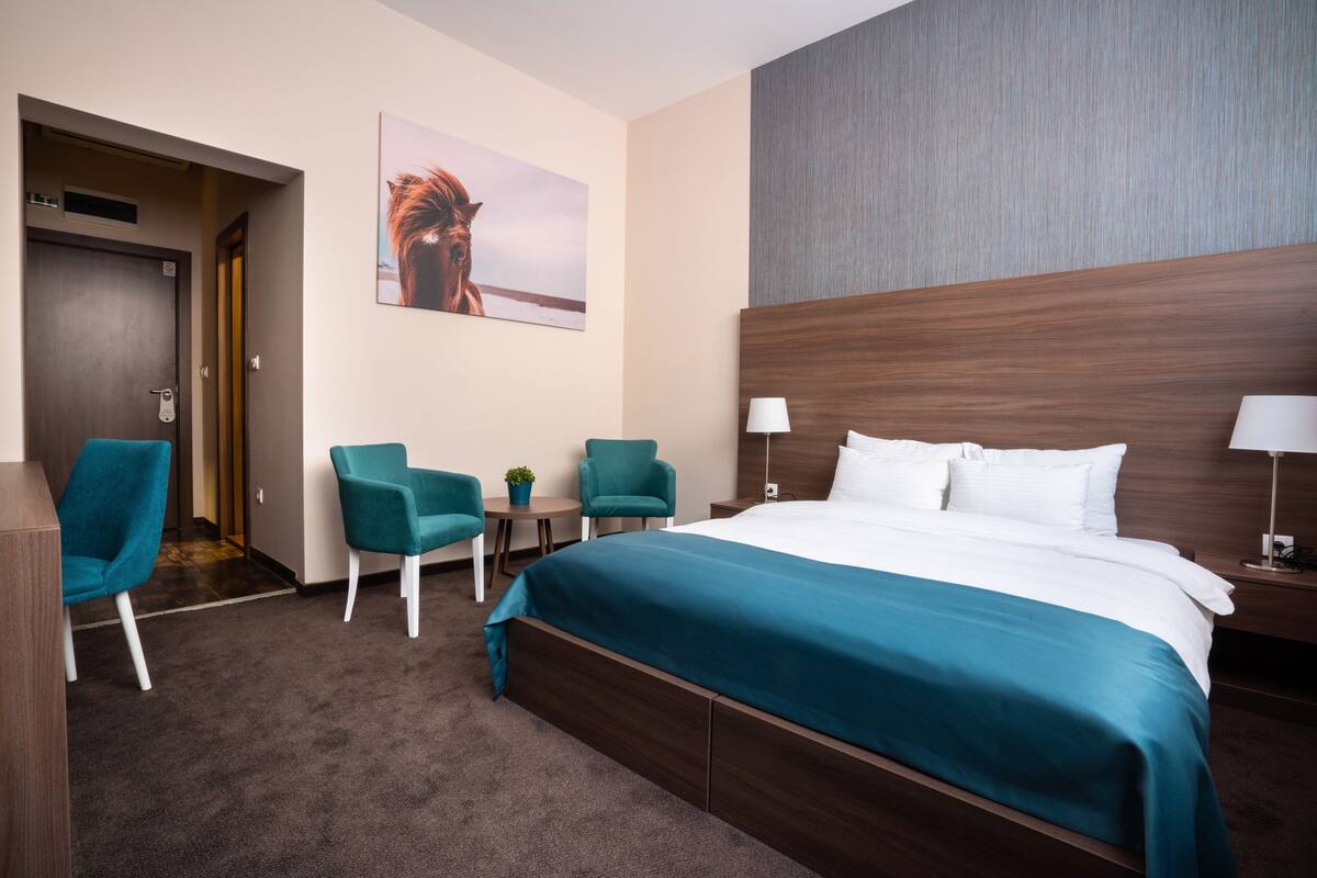 Ein Hotelzimmer mit einem großen Bett, zwei Stühlen, einem kleinen Tisch und einem Gemälde an der Wand.
