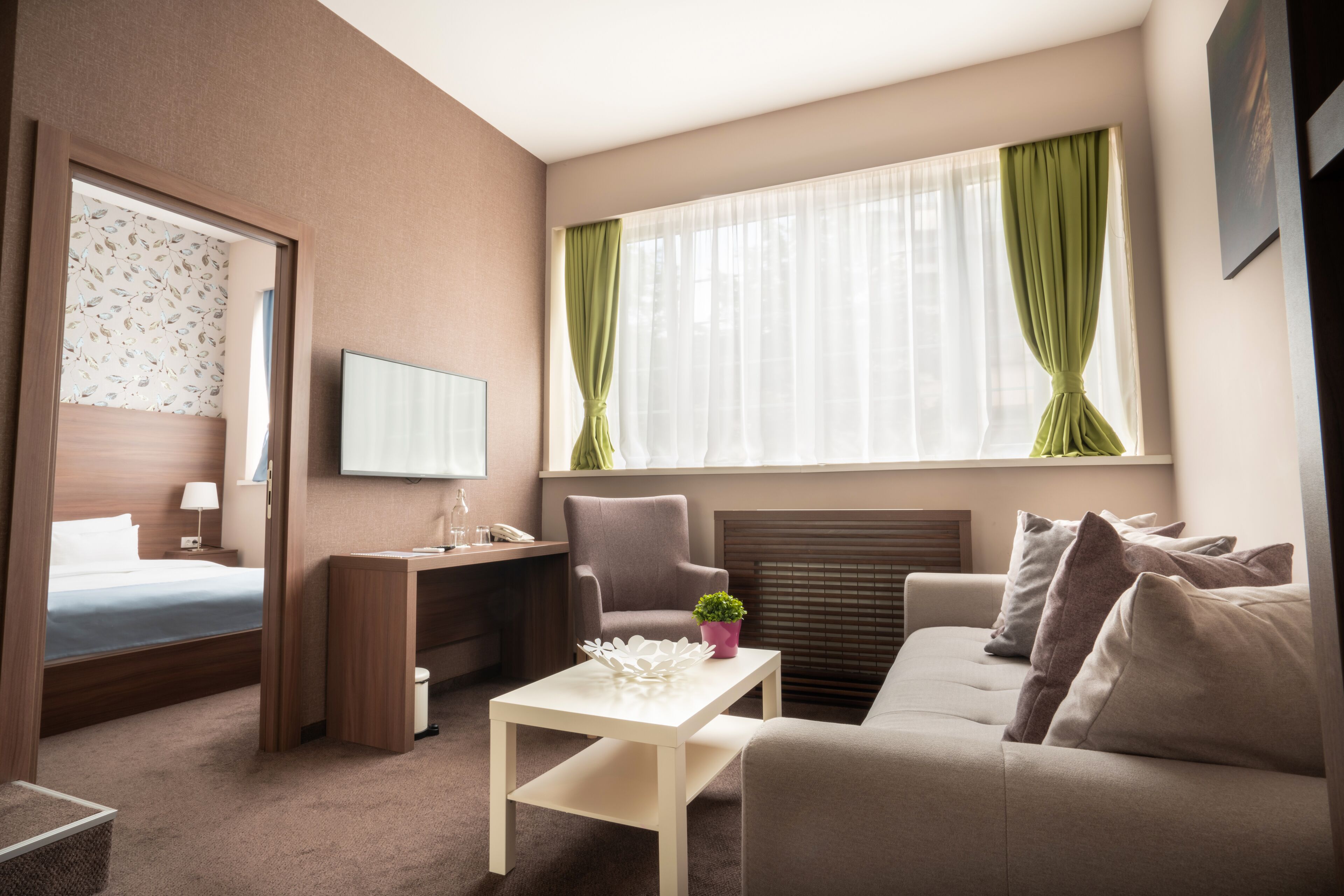 Een hotelkamer met een bed, bureau, bank, televisie en raam met gordijnen.