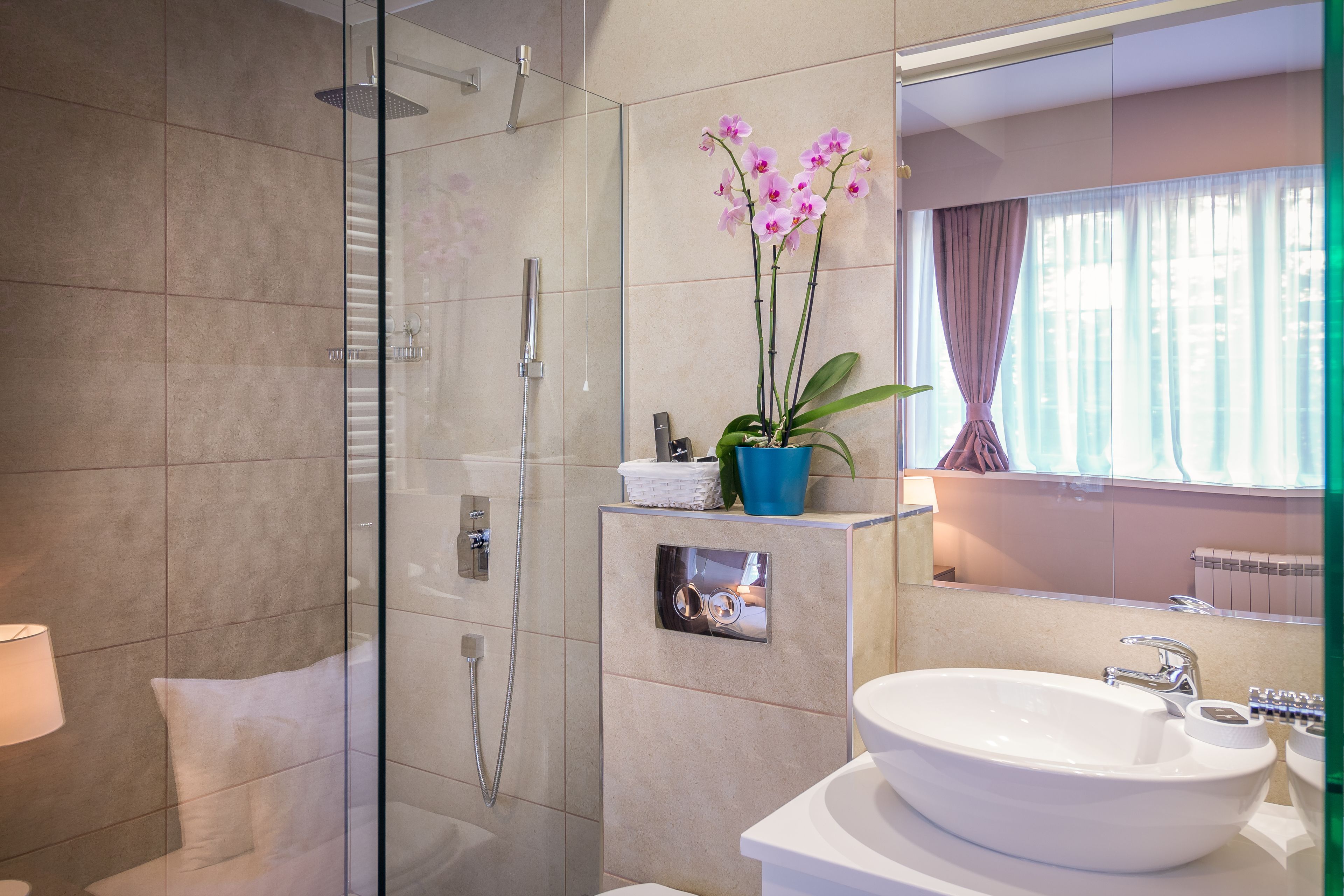 Un baño moderno con ducha de vidrio, lavamanos blanco y una orquídea en maceta.