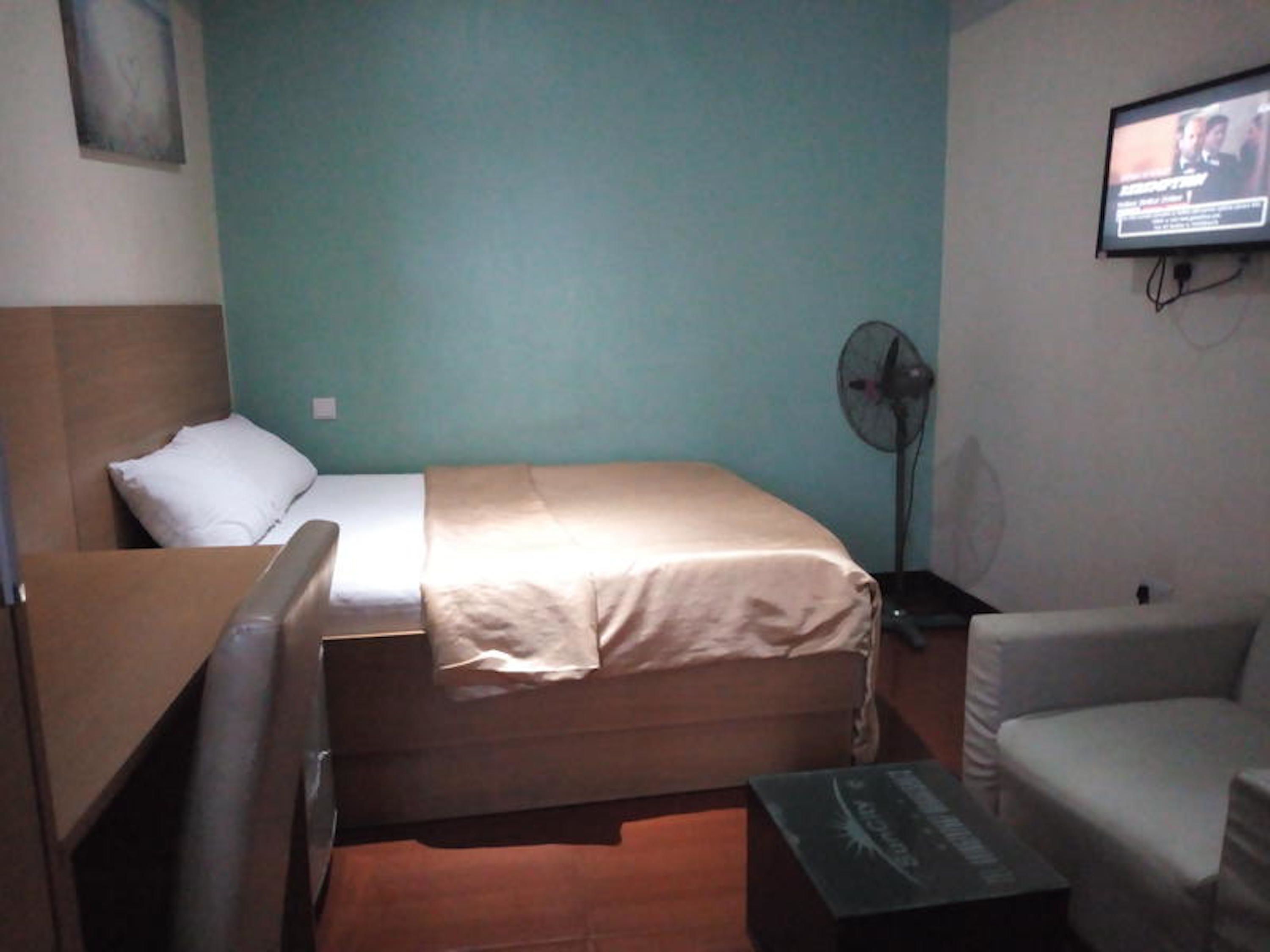 A room with a bed, a desk, a chair, a television, and a standing fan.