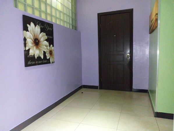 A hallway with a door, a wall-mounted poster with flowers, and a window with blinds.