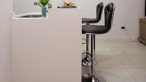 A modern reception area with a white counter, a vase with orange flowers, and a black bar stool. - New Kingston Premium Guest Apartment (Kingston)