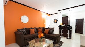 A living room with a brown sofa, orange accent wall, and a glass coffee table. - New Kingston Premium Guest Apartment (Kingston)