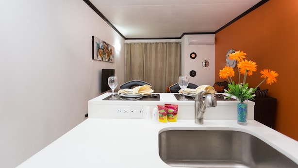 A compact kitchen with a white countertop, a stainless steel sink, and a dining area with chairs and a table set for two. - New Kingston Premium Guest Apartment (Kingston)