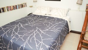 Een netjes opgemaakt bed met een donkerblauwe en witte spreideken, een wit kussen en een houten nachtkastje met een lamp.