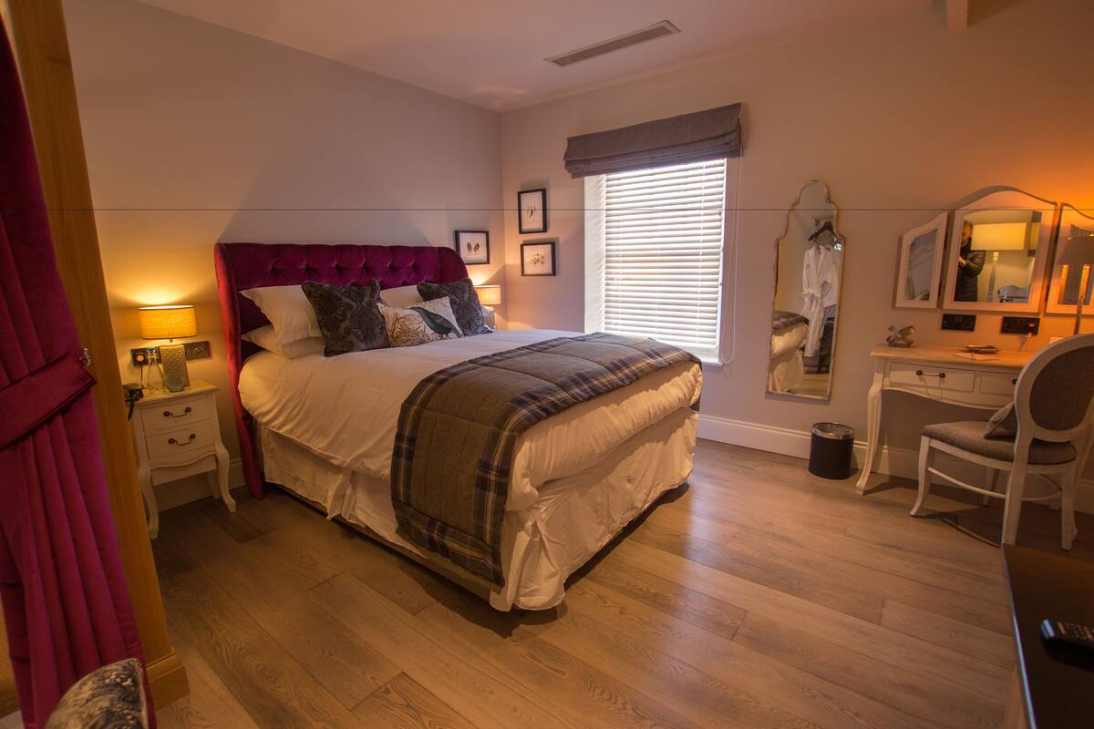 A bedroom with a bed, bedside tables, a dresser, a chair, and a window with blinds.