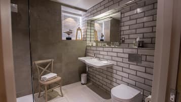 Un baño con pared de azulejos, un lavamanos, un inodoro y una ventana con persianas.