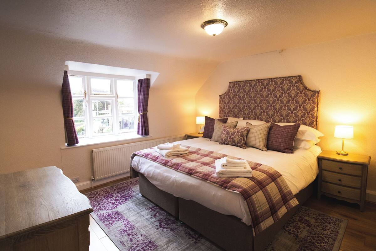 A bedroom with a large bed, bedside lamps, a window with curtains, and a radiator.