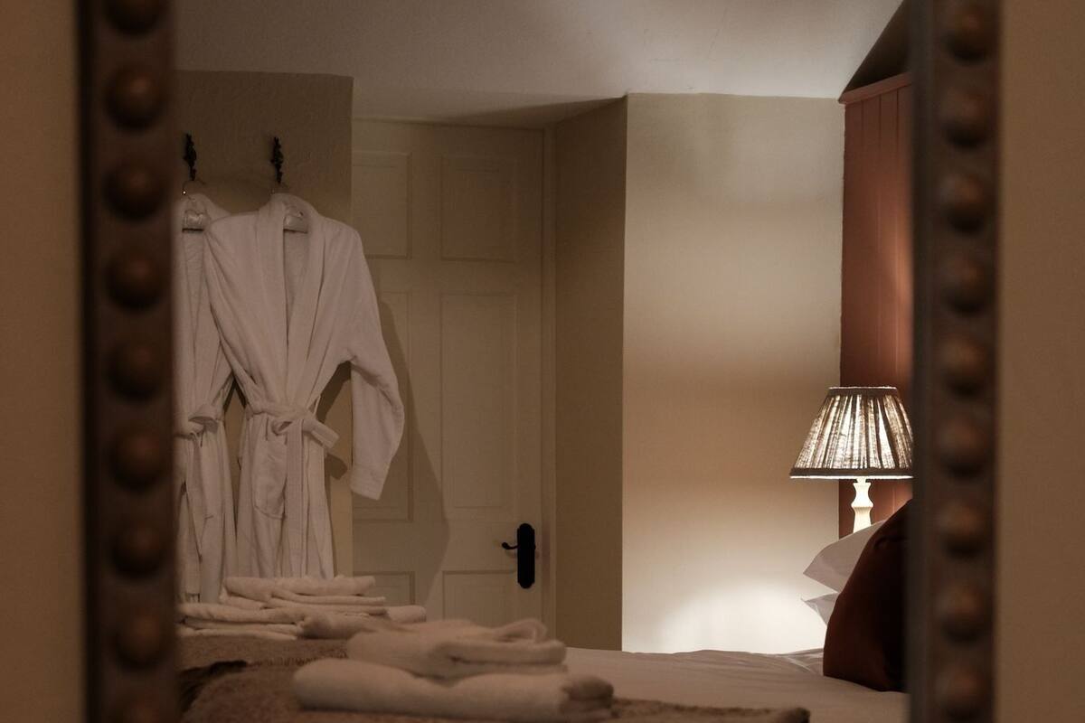 A hotel room with a bed, a bedside lamp, a mirror, and a robe hanging on the wall.