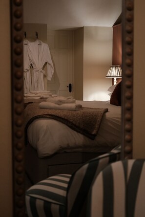A hotel room with a bed, a bedside lamp, a mirror, and a robe hanging on the wall. - The Peacock at Barlow (Dronfield)