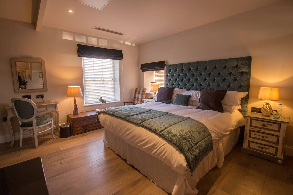 A bedroom with a large bed, a desk, a chair, and a nightstand with lamps.