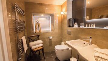 Un baño moderno con cabina de ducha de vidrio, una silla de madera, un inodoro y un lavamanos con espejo.
