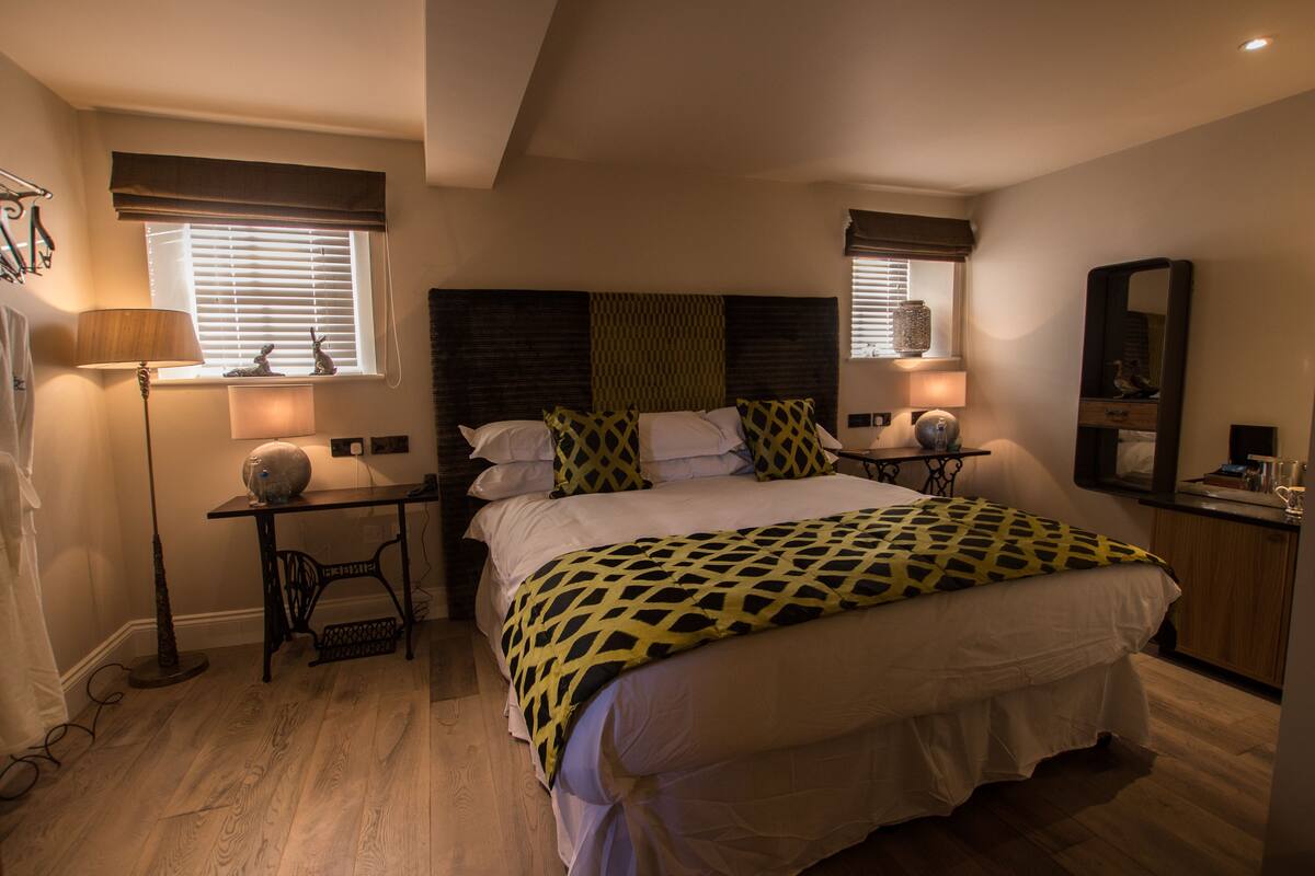 A bedroom with a large bed, two bedside tables with lamps, a dresser, and a mirror.