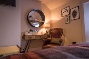 A room with a wooden desk, a leather chair, a round mirror, and framed artwork on the wall.