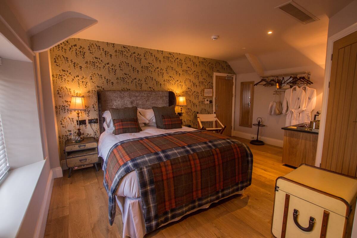 A bedroom with a large bed, a bedside table, a lamp, a dresser, and a suitcase.