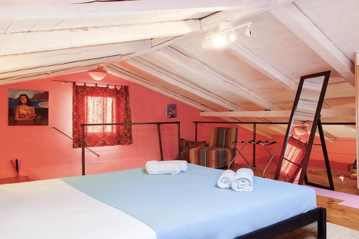 A bedroom with a bed, a window with curtains, a painting on the wall, and a mirror.