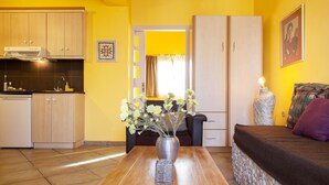 A compact living space with a kitchenette, a dining table with a vase, and a bed with a headboard. - Villa Kirki Apartments (Kefalonia)
