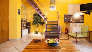 A compact living space with a wooden floor, a staircase, a dining area with a bowl of fruit, and a kitchen area. - Villa Kirki Apartments (Kefalonia)