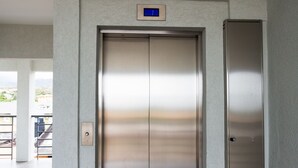 Un ascensore moderno con finiture metalliche, situato in un corridoio con pavimento piastrellato e pareti di colore chiaro.