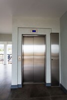 A modern elevator with a metallic finish, located in a hallway with tiled flooring and light-colored walls.