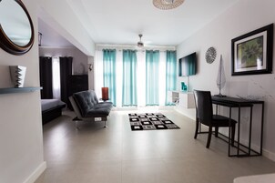 A modern living room with a sofa, a dining table with chairs, a TV, and a large window with curtains.