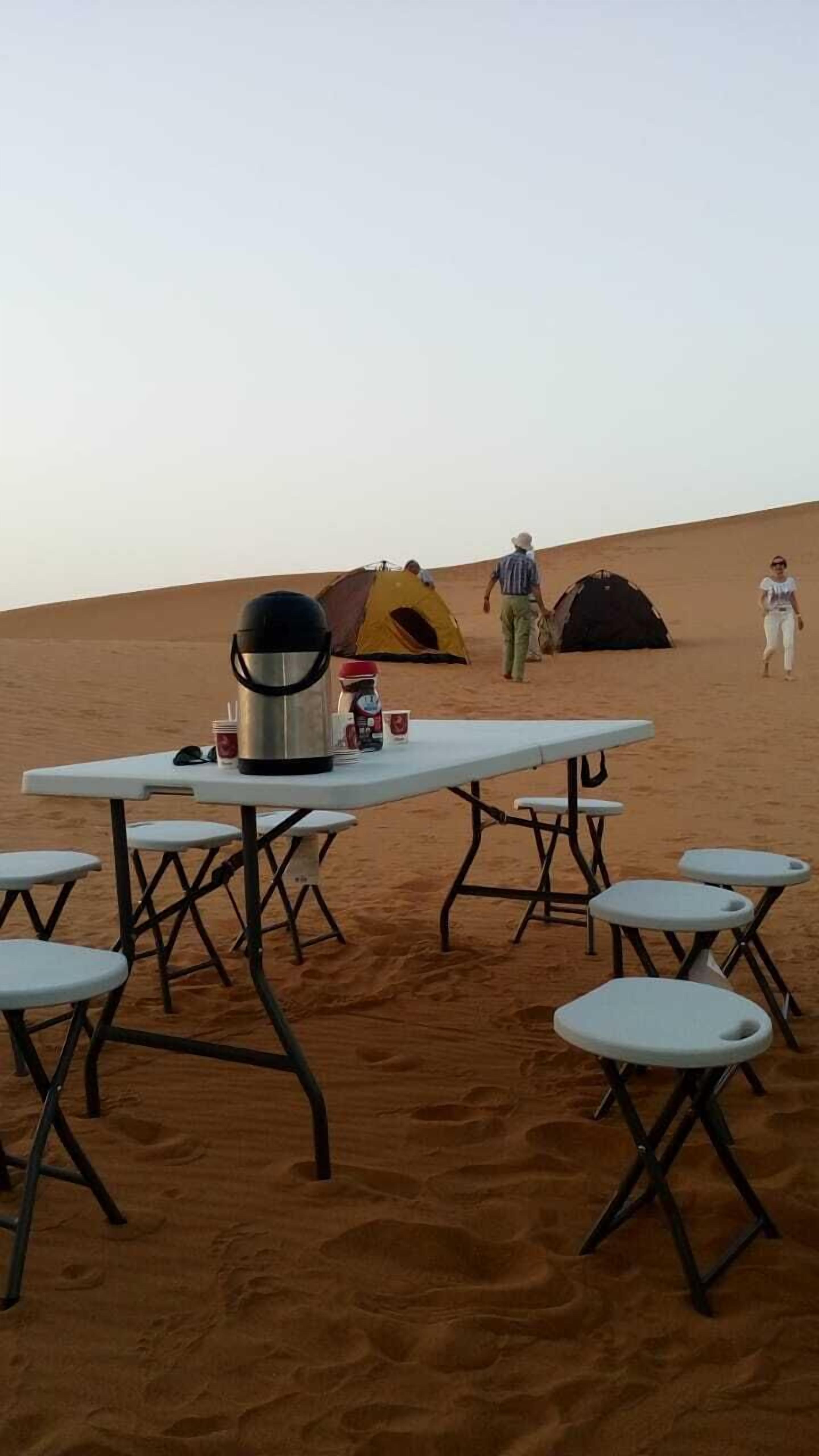A desert campsite with a table and chairs, a tent, and a cooler.