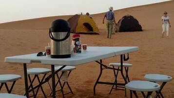 A desert campsite with a table and chairs, a tent, and a cooler.