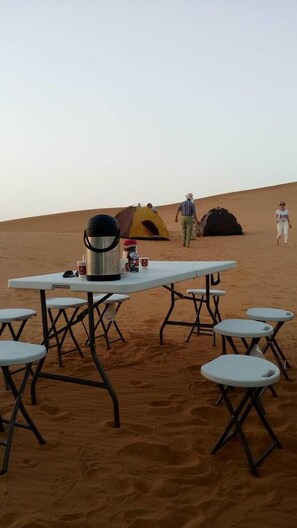 A desert campsite with a table and chairs, a tent, and a cooler.