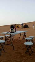 Un campamento en el desierto con una mesa, sillas, una tienda de campaña y un enfriador.