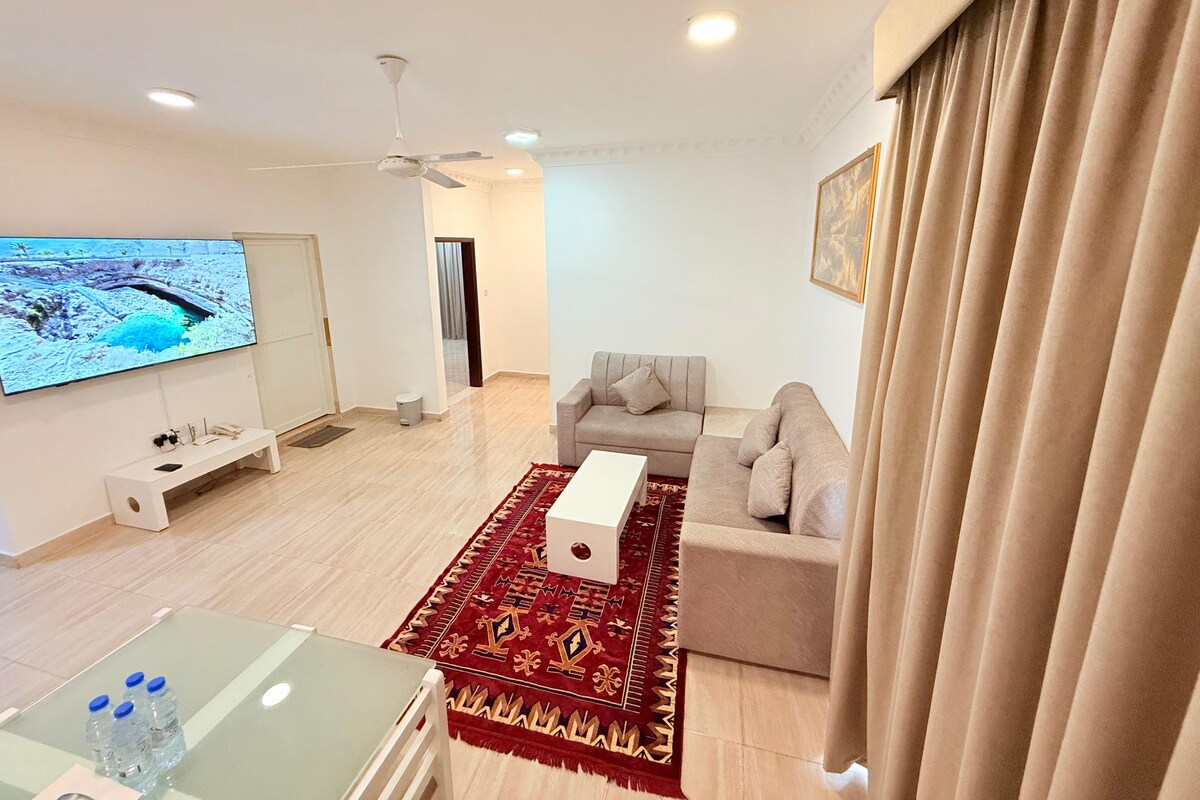 Un salon moderne avec un téléviseur à écran plat, un canapé, une table basse et un tapis à motifs.