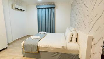 Ein Hotelzimmer mit einem Bett, einem Deckenventilator, einer Klimaanlage, einem Fenster mit blauen Vorhängen und einer Wand mit Marmoroptik.