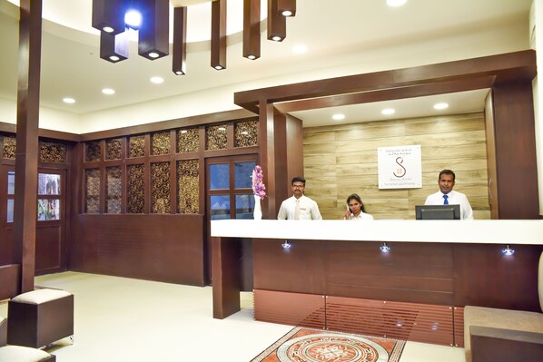 A reception desk with three staff members, a wooden wall with a sign, and a patterned carpet.