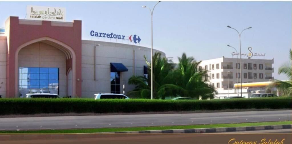 A Carrefour store with a large arch entrance, a parking lot, and a building with a sign for 'Salalah Gardens Mall' in the background.