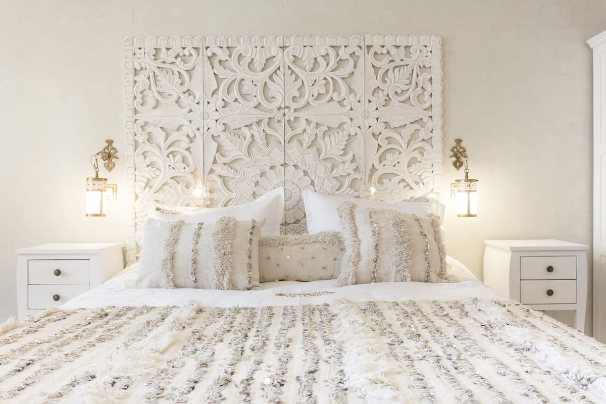 Een slaapkamer met een groot bed, een versierd hoofdbord, twee nachtkastjes met lampen en een decoratief wandpaneel.