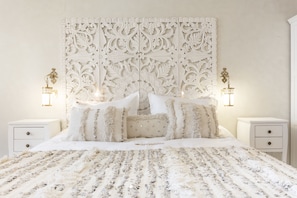 A bedroom with a large bed, ornate headboard, two bedside tables with lamps, and a decorative wall panel.