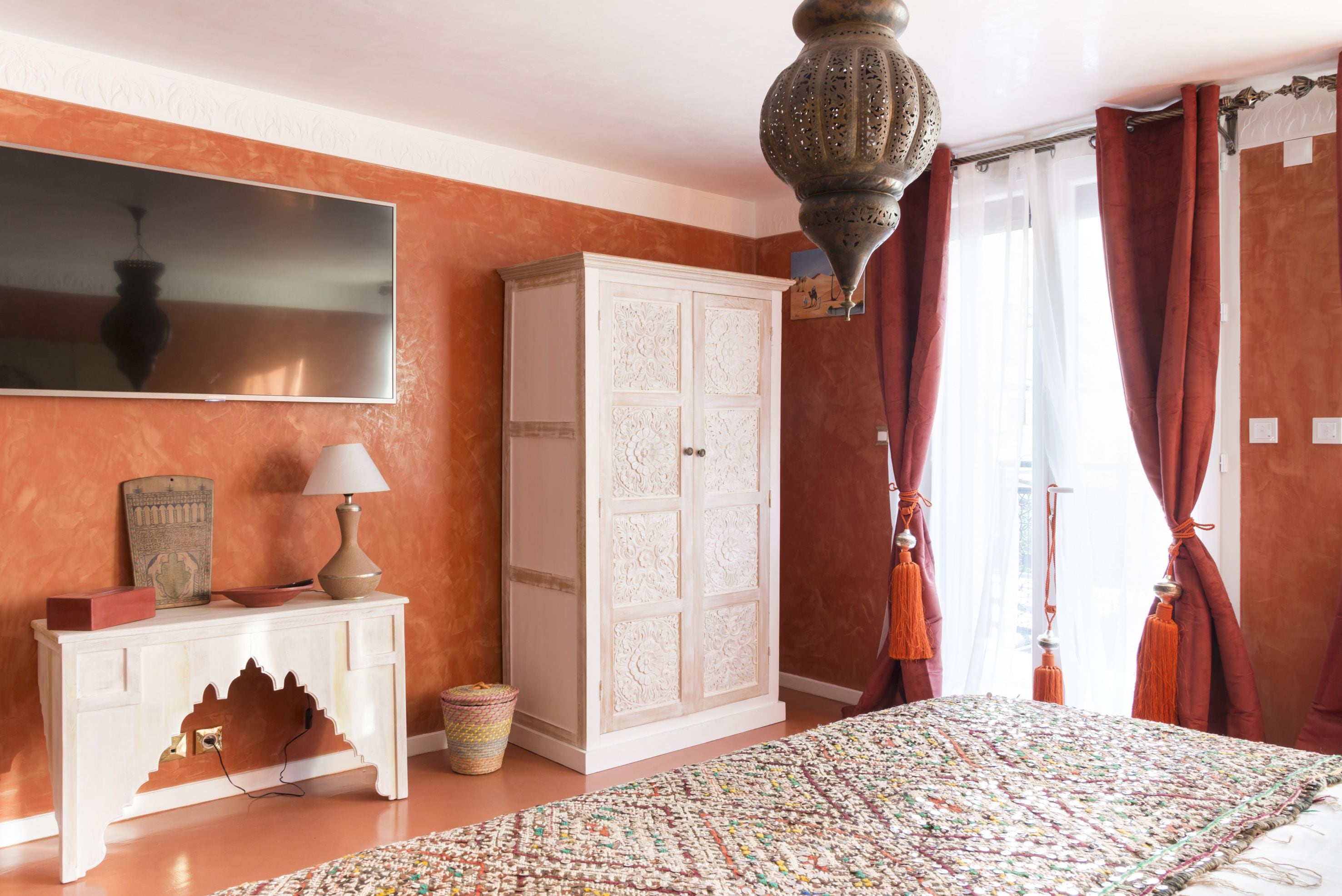 Un dormitorio con una cama grande, un armario blanco, un televisor en la pared y una lámpara colgante.