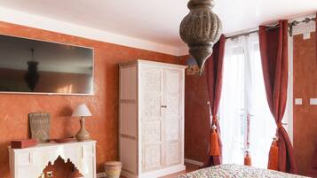 Un dormitorio con una cama grande, un armario blanco, un televisor en la pared y una lámpara colgante.