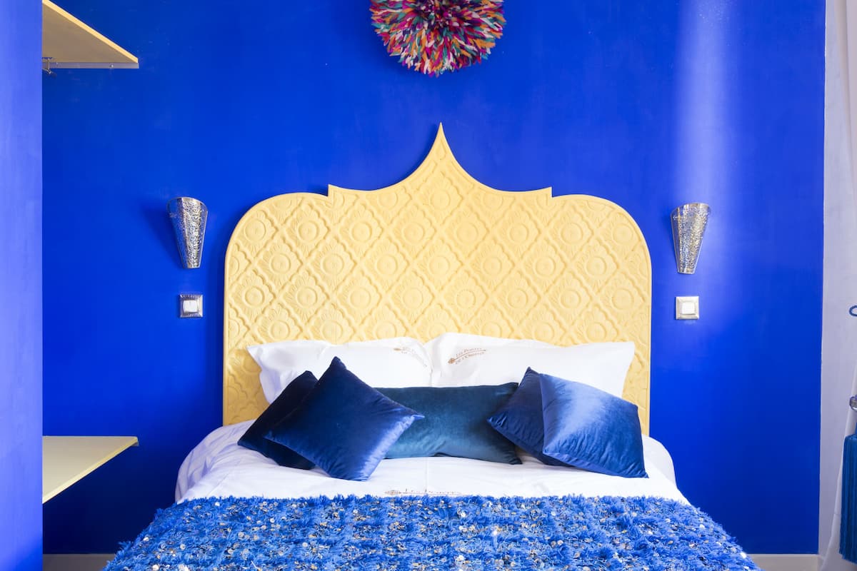 Een bed met een geel hoofdeinde, blauwe wanden en een bloemendecor in blauw op het bed.